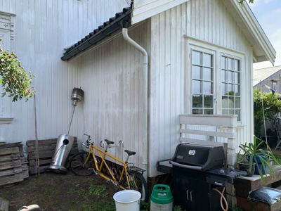 Fotografi av en hvit, trepanelert bygning sett fra bakgårdssiden med gress, sykkel og grill i forgrunnen.