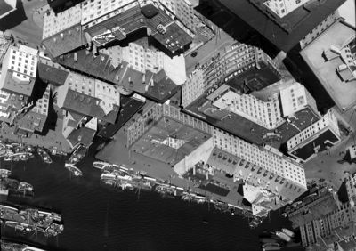 Sort-hvitt flyfoto som viser en bydel med mange bygninger, gater og et havneområde med båter.