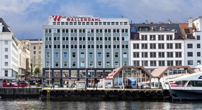 Fotografi av Wallendahl-hotellet sett fra kaien i Oslo, med omgivende bygninger og vann i forgrunnen.