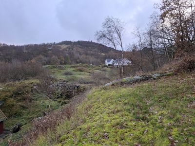 Fotografi av et naturområde med en ås i bakgrunnen og to hvite hus synlige på fjellet.
