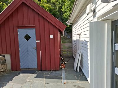 Fotografi av en rød skur med blå dør og en hvit bygning ved siden av, sett fra bakkenivå.