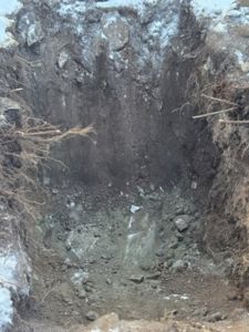 Fotografi av en utgravd grøft eller hull i bakken, sannsynligvis for å undersøke grunnforhold eller for å grave fundament.