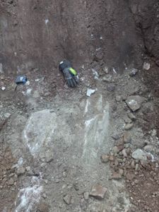 Fotografi av en utgravd grøft eller gruve med en handskede og et målebånd som skala.