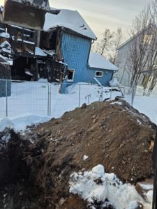 Fotografi av en blå hytte som har vært utsatt for brannskader, med en stor jordhaug i forgrunnen.