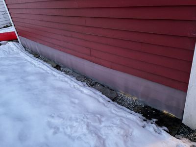 Fotografi av en bygning med rød fasade og hvit grunnmur, sett fra bakkenivå med snø på bakken.