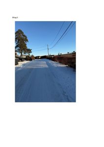 Fotografi av en snødekket vei med hus i bakgrunnen.