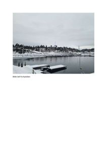 Fotografi av en havn eller kai med snødekkede båter og land i bakgrunn.