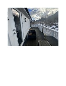 Fotografi av en terrasse med hvit fasade, dør og utsikt over et snødekt landskap.