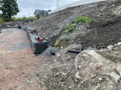 Fotografi av en byggeplass som viser en delvis ferdig murvegg, grøfting og rørlegging.