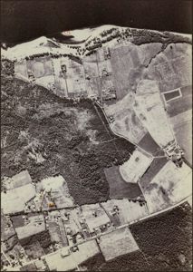 Flyfoto eller luftfoto av et område med skog, åker og bebyggelse, med overlagte røde markeringer og tekst som indikerer en byggesak.