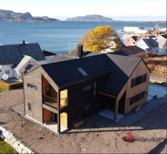 Fotografi av en nybygd eller under oppføring stående hus sett fra luften, med omgivende natur og nabolag.