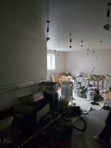 Fotografi av et rom under renovering eller byggeprosess, med synlig utstyr, materialer og delvis ferdigbehandlede vegger.