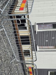 Fotografi av en bygning under oppføring eller renovering, med fokus på fasaden, vinduer og grunnmur. Bildet er tatt fra bakkenivå og viser en del av bygningen omgitt av sikkerhetshekk.