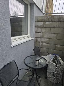 Fotografi av en liten terrasse eller balkong med møbler, en vegg med vindu og en blokkvegg.