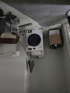 Fotografi av et rom under renovering eller etter flytting, med vaskemaskin, møbler og byggemateriale.