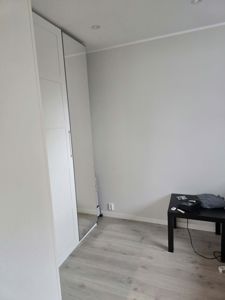 Fotografi av et innvendig rom (sannsynligvis soverom eller stue) med hvite skap, gulv og en liten bord.