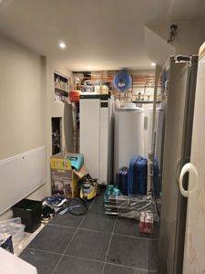 Fotografi av en teknisk rom (kanskje kjeller eller teknisk rom) med varmeanlegg, rør og utstyr.