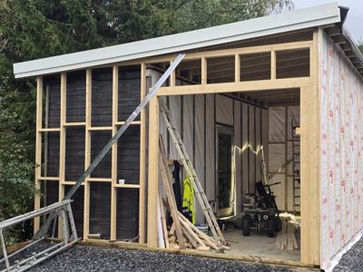 Fotografi av en bygning under oppføring, som viser den ferdige takkonstruksjonen, rammen og isolasjonen på veggen.