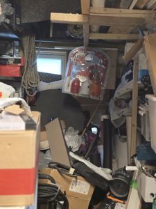 Fotografi av et svært kassert lager eller garasje, med utstyr, kasser og materialer i forgrunnen og bakgrunnen.