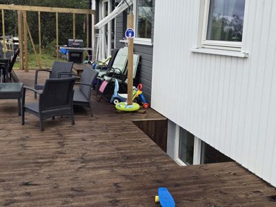 Fotografi av en uteplass med terrasse, møbler og en del av en hvit panelt husfasade.