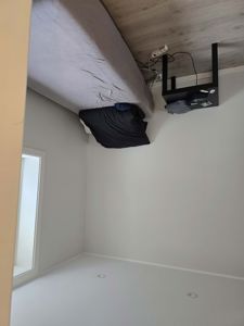 Fotografi av et lite soverom med en seng, et nattbord og et vindu.