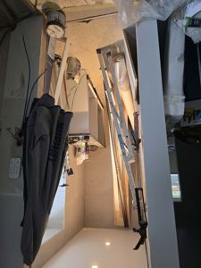 Fotografi av et rom under renovering eller bygging, med byggematerialer, trapp og klær synlig.