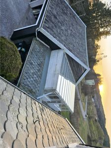 Fotografi av en bygning sett fra en høyde, som viser takkonstruksjon, en tilbygget veranda og omgivelser.