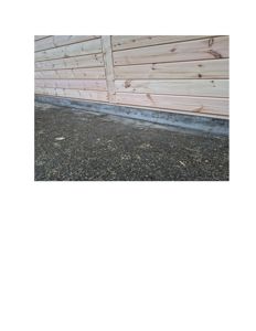 Fotografi av en bygning som viser detaljen ved grunnmur og fasade. Bildet viser en betongfundament som går under en trepanelfasade.