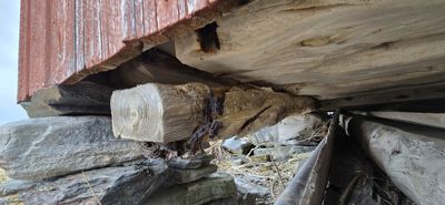 Fotografi av en gammel bygning som viser detaljer i fundamentet, inkludert steinmur, tømmer og en rotting.