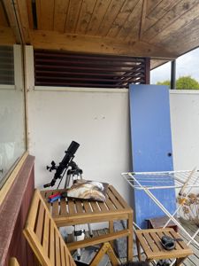 Fotografi av en uteplass eller balkong med en teleskop, en blå dør og en tørkestativ.