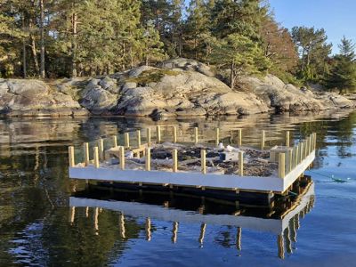 Fotografi av en ferdig eller nesten ferdig bygget plattform (kai eller brygge) i vann, med en kystlinje i bakgrunnen.