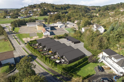 Luftfoto av et nybygd anlegg med flere bygninger, omgitt av grønt og nabostruktur.