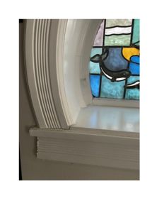 Fotografi av en hvit, profilert vindusramme med et farget glasspanel (mosaikkglass) som viser en hval.