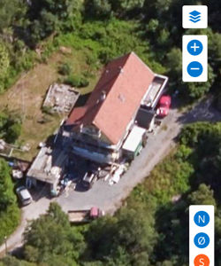 Luftfoto av en bygning med rødt tak, omgitt av vegetasjon og parkerte biler.