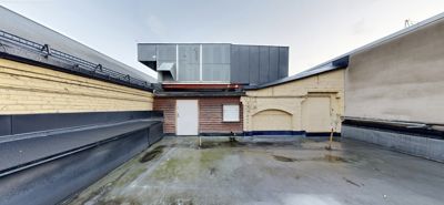 Fotografi av en takterrasse eller takflate med tilhørende fasader og en moderne tilbygg i bakgrunnen.