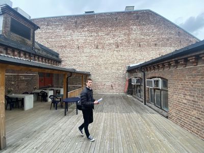 Fotografi av en uteplass eller terrasse med tredekk, omgitt av murvegger og et takverk. En person går på dekken.