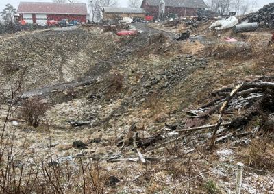 Fotografi av et utendørs område med snø, en rød bygning i bakgrunnen og en uordnet terrengformet forgrunn.