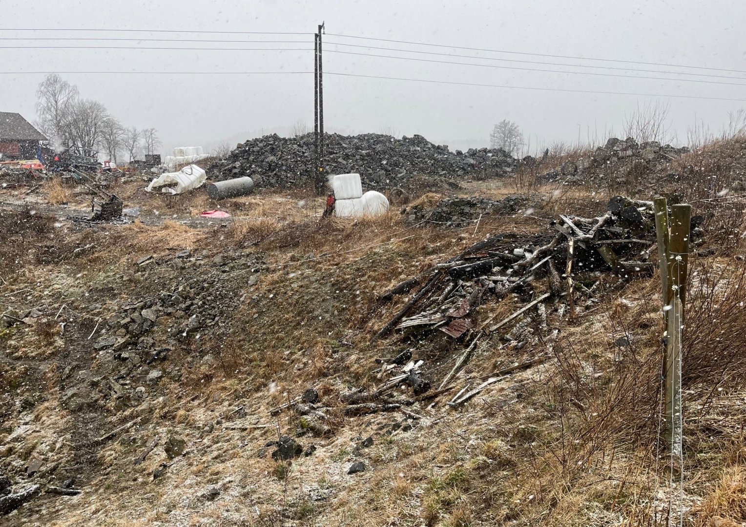 Fotografi av et bygge- eller renovasjonstomt med snø, avfall og en del av en bygning i bakgrunnen.