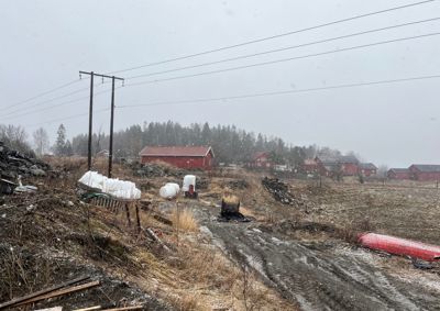 Fotografi av et utendørs område med en vei, en rød bygning i bakgrunnen og snøfall.