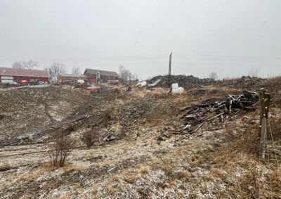 Fotografi av et utendørs område med snø, grus, og noen bygninger i bakgrunnen.
