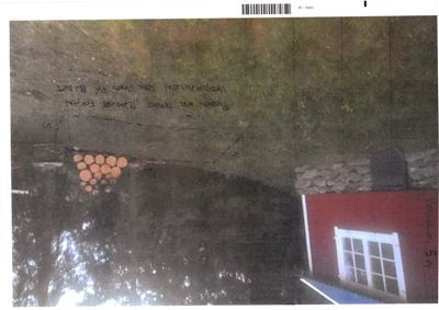 Fotografi av en rød bygning med hvit ramme rundt vinduet, sett fra siden. Bildet viser også en del av grunnen, en haug med tømmer og en håndskrevet notis om 'Vedutleie 5A'.