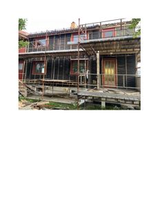 Fotografi av en toetasjes bolig under ombygging eller renovering, med stålskelett og fasadebeskyttelse.