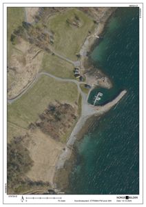 Flyfoto eller ortofoto av et kystområde med vei, bebyggelse og en brygge.