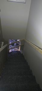 Fotografi av en trapp med mørke trinn, lyse vegger og en delvis montert håndtak.