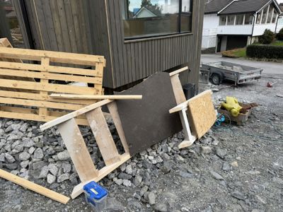 Fotografi av en byggeplass med en ferdig fasade på en bygning i bakgrunnen, mens det ligger byggematerialer (pall, panel, rammer) på forgrunnen.