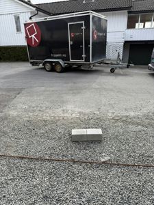 Fotografi av en svart trailer parkert på en grusflate foran en hvit villa.