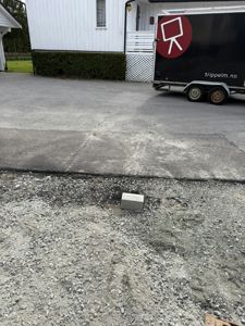 Fotografi av en hvit villa med en trailer parkert foran. Bildet viser fasaden, en del av hagen og en asfaltert vei.