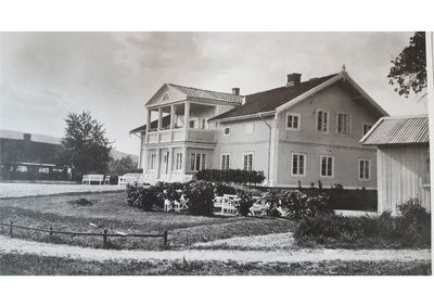 Et svart-hvitt fotografi av en stor, toetasjes bygning (sannsynligvis et gammelt landbrukseiendom eller gård) sett fra fronten.
