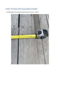 Fotografi av en gul målebånd som ligger på en gråtre-terrasse. Bildet illustrerer en måling av terrassens lengde.