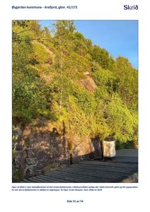 Fotografi av en bratt fjellskrent med vegetasjon og en takkonstruksjon i forgrunnen.